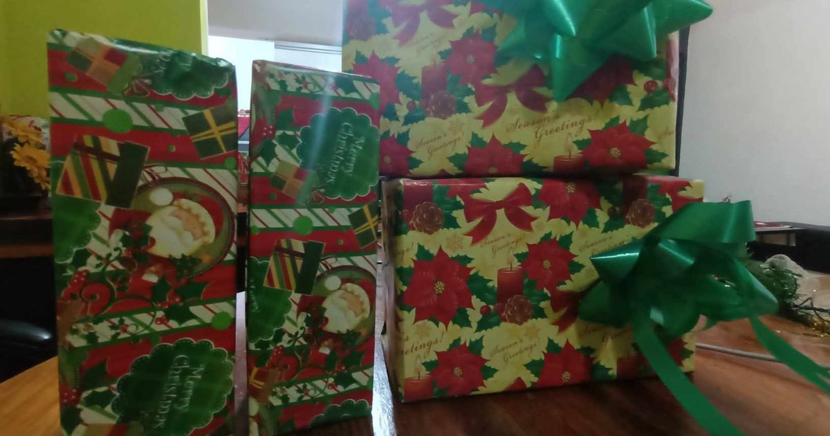 Four Christmas presents in red, green and poinsettia wrapping paper with green bows, stacked on a wooden table